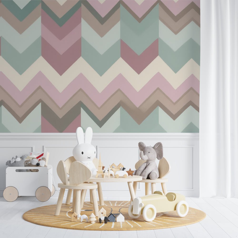 Close-up of geometric chevron mural wallpaper pattern in pastel pink and sage green with Scandinavian style children's furniture